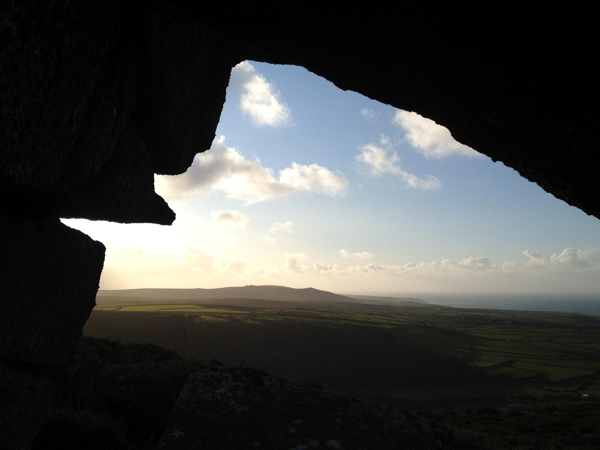 Sunlit Cornish moorland and distant sea seen through a dark stone opening